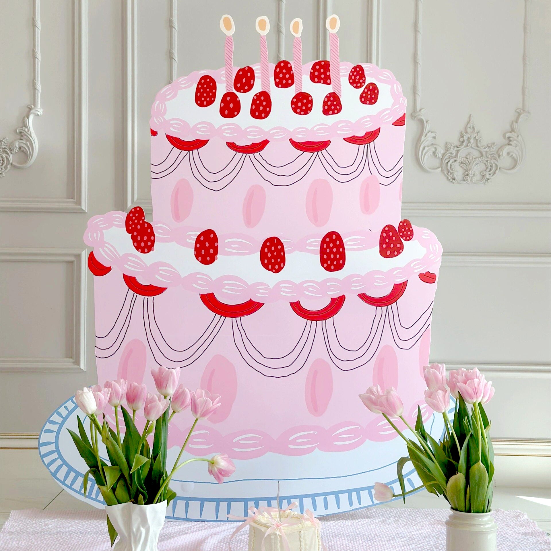 A whimsical illustration of a large, pastel pink, two-tier cake adorned with red decorations and topped with five lit candles. The background features an elegant, ornate wall, accented by Dongguan Quanjia Trade Co.,ltd's 5ft Happy Birthday Cake Foam Board Cutcout Props Standee for party celebrations, while pink tulips in vases are placed in front of the cake.