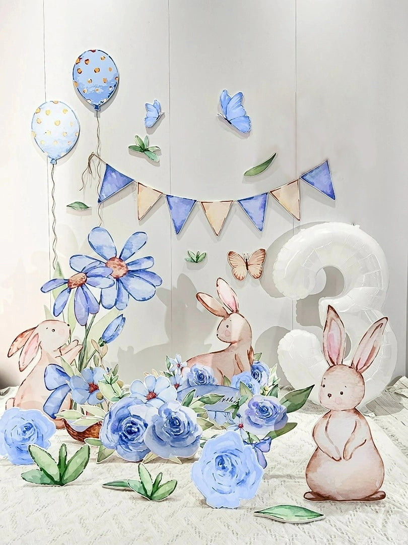 A whimsical birthday setup features pastel-colored bunny illustrations, large blue flowers, butterflies, and a "3" balloon. The **Blue Garden Bunny Flower Standee Cut Out Foam Board Decoration Set of 30 by Dongguan Quanjia Trade Co., Ltd** adds an extra touch of magic alongside a garland with blue and beige triangles and polka-dotted balloons hanging in the background, creating a charming and festive scene.